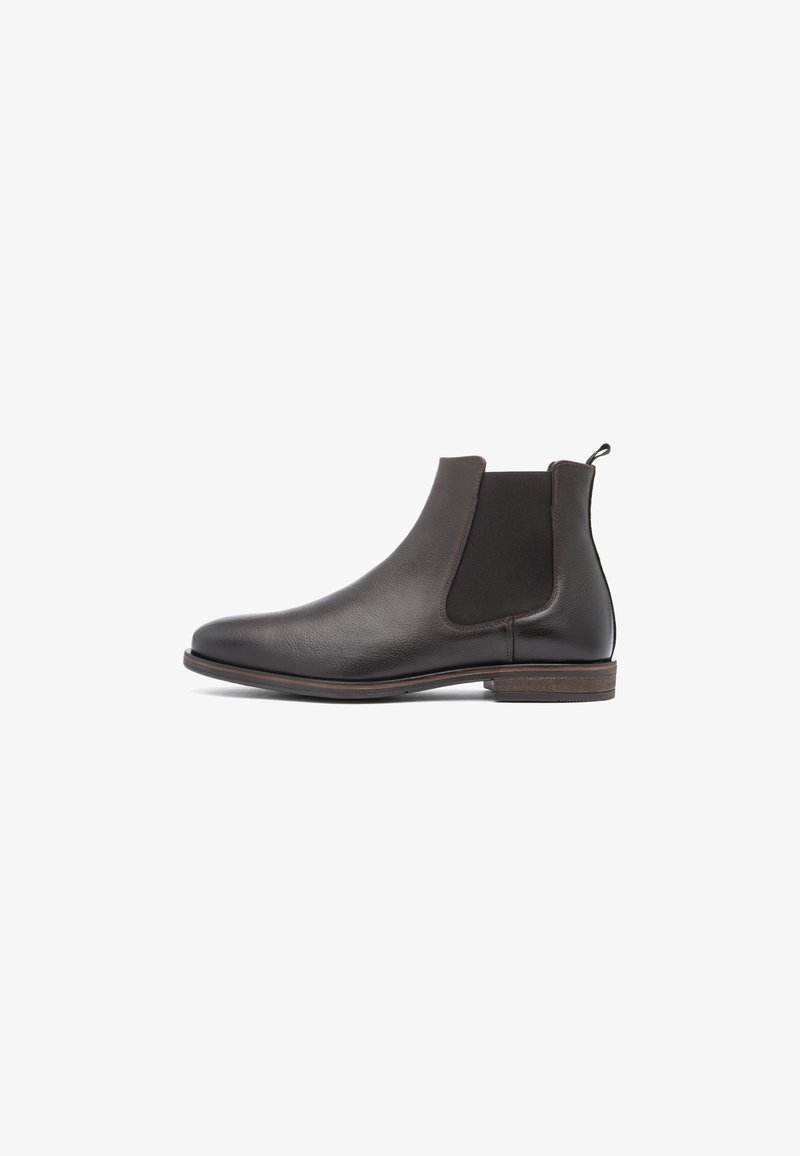 Bottine Chelsea en cuir noir avec panneaux latéraux élastiques, languette de tirage au talon et semelle en bois basse empilée sur fond blanc.