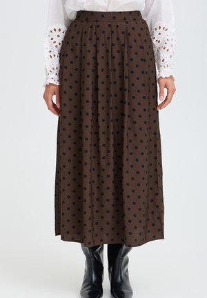 Jupe midi marron à pois noirs portée avec un chemisier blanc à manches en dentelle et des bottines en cuir noir sur fond blanc.