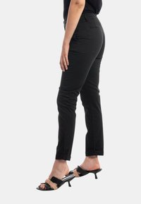 Pantaloni neri a sigaretta con una texture liscia, dotati di vita aderente e risvolti. Abbinati a sandali con tacco a blocco neri e nudi.