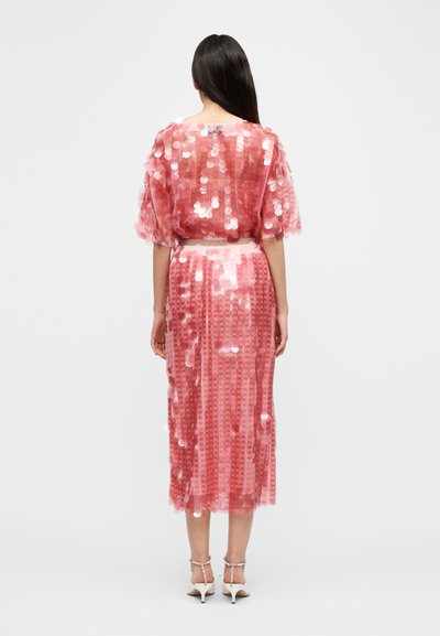 Robe rose à sequins avec des manches courtes et bouffantes et une longueur midi. Dotée d'une superposition transparente et d'une ceinture cintrée.