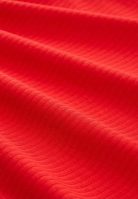 Textilgewebe in lebhaftem Rot mit einem strukturierten, wellenförmigen Rippmuster. Glatte Oberfläche mit einheitlicher Farbe und Tiefe.