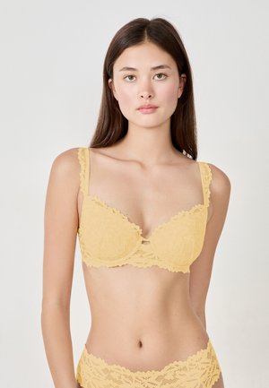 Reggiseno in pizzo giallo con bordo a scallop, supporto con ferretto e un piccolo dettaglio a chiave nella parte anteriore. Le spalline regolabili contrastano con il design.