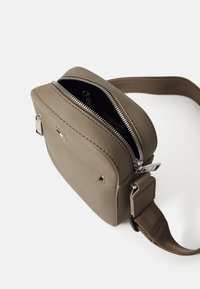 Brun texturerad läder crossbody-väska med dragkedjestängning, justerbar rem och metallic detaljer. Inredningen kan inte ses.