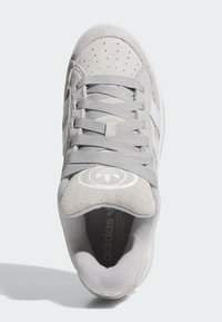 Grå semsket sneaker med hvite striper, rund tå, teksturert tunge og logo. Har grå lisser og perforert overdel for pusteevne.