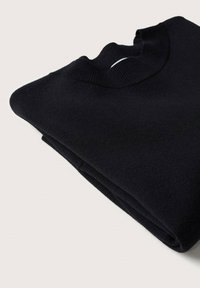 Pull en maille noir plié avec un col rond côtelé sur un fond clair.