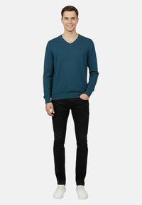 Maglione a V verde acqua in morbido tessuto lavorato a maglia, abbinato a jeans neri e sneakers bianche. Il maglione presenta polsini e orlo a coste per una maggiore texture.