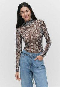 Langarm, aansluitend top in doorschijnende slangenprintstof met een hoge hals. Gecombineerd met lichtblauwe, relaxte denim jeans.