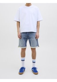 Maglietta bianca in cotone, pantaloni corti in denim blu con risvolti, sneakers blu e calze bianche con strisce blu e nere. Outfit semplice e casual.