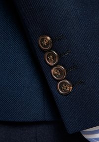 Rękaw granatowego garnituru o pionowym żebrowanym wzorze, z czterema okrągłymi brązowymi guzikami o skomplikowanych detalach, przyszytymi czarną nitką.