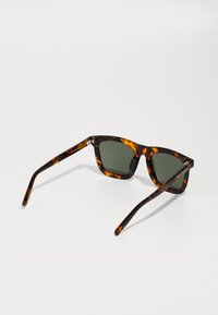 Tortoiseshell sunglasses with green lenses. Angular frame, slim arms, and subtle branding on the temple. Glossy finish enhances texture.