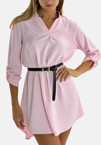 Roze jurk met lange mouwen en een kraag, getailleerd met een zwarte riem. Zachte textuur met een iets losse pasvorm en opgerolde mouwboorden.