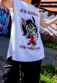 Camiseta sin mangas blanca con un diseño gráfico de la cabeza de un lobo, lengua roja, texto adornado "ED HARDY" y "LOS ÁNGELES" en colores contrastantes.