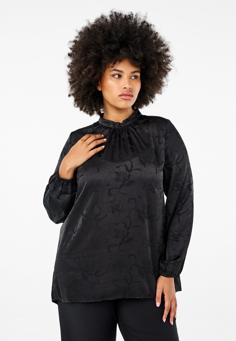 Blusa nera con motivo jacquard floreale, colletto alto con pieghe, maniche lunghe con polsini elasticizzati e vestibilità morbida. Texture satinata liscia.