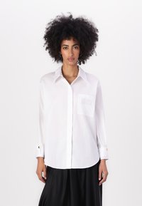 White button-up shirt with a pocket, long sleeves, and gold button accents. Smooth texture and classic collar design.