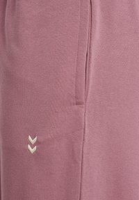 Lys lilla bomulds joggers med en blød tekstur, sidelomme og et lille hvidt broderet chevron-logo på venstre side.