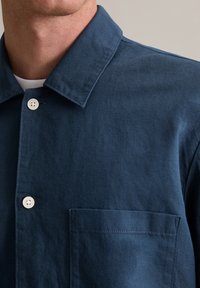 Marineblauwe overhemd met knopen, gemaakt van textured stof, met een puntkraag, borstzak en witte knopen.