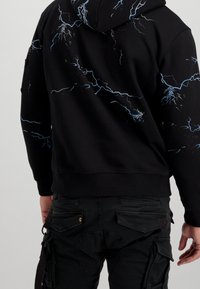 Czarna bluza z kapturem z niebieskimi wzorami błyskawic, wykonana z miękkiego materiału, z ściągaczami przy rękawach. W zestawie czarne spodnie cargo z kieszeniami.