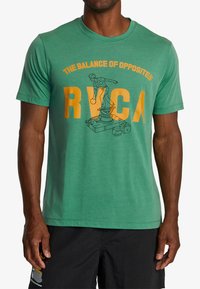 Green cotton t-shirt featuring a graphic print of a statue and the text "THE BALANCE OF OPPOSITES" and "RVCA" in yellow. Short sleeves.