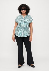Short-sleeve, button-up shirt with a teal and white geometric pattern paired with black flared pants and flat black shoes.