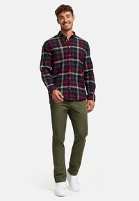 Rood, marineblauw en beige geruit flanellen overhemd met een knoopsluiting, gecombineerd met olijfgroene broek en witte sneakers.