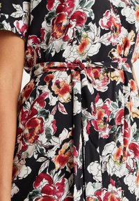 Robe fleurie en tissu noir ornée de grandes fleurs rouges, crème et vertes. Comprend une ceinture nouée à la taille et des manches courtes, avec des accents de boutons.