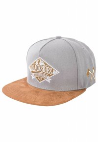 Gorra gris con visera de ante marrón. Presenta un logo en blanco y dorado con gráficos de montañas en la parte delantera. Incluye un acento decorativo en el lateral.