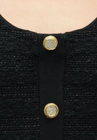 Μαύρο υφασμάτινο υλικό με υφή και οριζόντιες ρίγες, με κεντρικό κουμπί που διαθέτει χρυσές λεπτομέρειες και κρυστάλλινες διακοσμήσεις.