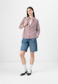 Red and white striped button-up shirt, blue denim shorts, white socks, black heeled shoes; model standing against a white background.