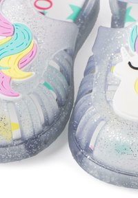 Clear, glittery sandals with a translucent design. Features a unicorn accent and colorful, textured hair detail. Flexible and breathable material.