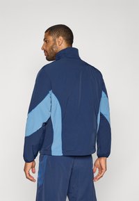 Chaqueta cortavientos navy con detalles en azul claro, que presenta un cuello alto, puños elásticos y un diseño de ajuste relajado para mayor comodidad.