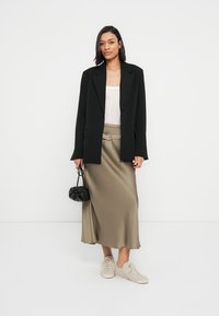 Μαύρο σακάκι πάνω από λευκό τοπ, σετ με μπεζ μίντι φούστα με ζώνη, ανοιχτόχρωμα αθλητικά παπούτσια και μικρή μαύρη τσάντα.