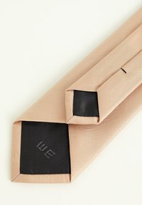 Cravat din mătase bej cu textură diagonală în relief, având o căptușeală neagră solidă și un logo brodat în colț. Vârfuri triunghiulare.