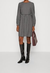 Rutig svart och vit klänning med långa ärmar, rund halsringning och elastisk midja, tillsammans med knähöga svarta stövlar och en vinröd väska.