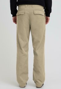 Khaki värvi püksid sirge lõikega, kahe tagataskuga ja siledast kangast, koos musta tekstuurse pika varrukaga särgiga.