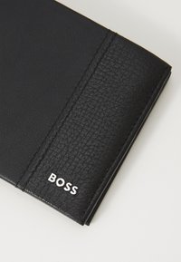 Black leather wallet with a textured surface, featuring a silver "BOSS" logo and visible stitching along the edge.
