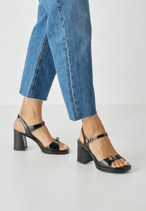 Zwarte glanzende leren sandalen met hak en een blokvormige vierkante hak, verstelbare enkelriem, open teenontwerp en metalen accenten.