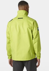 Chaqueta impermeable de color amarillo brillante con cuello alto, yugo trasero y rayas de acento negras. Cuenta con puños elásticos y un parche con el logotipo en la manga.