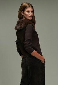 Donkerbruin sweater met een met bont gevoerde capuchon, met een ontspannen pasvorm, geribde manchetten en gecombineerd met zwarte corduroy broek.