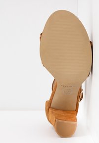 Sandale en suede marron avec un talon bloc, présentant une semelle texturée, une sangle réglable et un bout plat arrondi. Taille 37 indiquée sur la semelle.