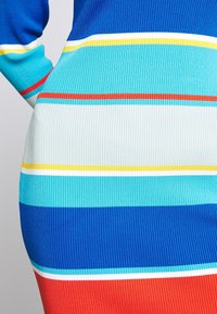 Gros plan d’un tissu tricoté côtelé avec des rayures horizontales en bleu, rouge, blanc, jaune et turquoise sur un vêtement ajusté.