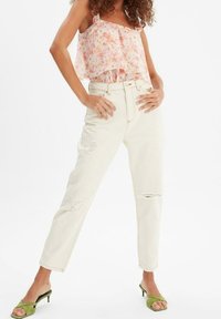 Vaqueros blancos desgastados de cintura alta y piernas rectas, combinados con una blusa rosa de flores y sandalias de tacón verde.