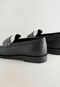 Mocassins en cuir noir et blanc avec une finition lisse, des détails cousus et un léger talon. Design minimaliste avec une tige accentuée.
