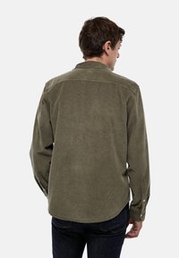 Chemise en velours côtelé vert olive avec un empiècement au dos, des poignets à boutons et un ourlet arrondi. Présente une texture côtelée verticale. Aucune vue de face montrée.