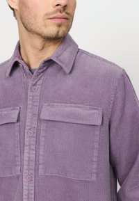 Paarse corduroy shirt met een gestructureerd oppervlak, voorzien van een kraag, twee borstzakken en knoopsluiting. Knopen zijn in bijpassende kleur.