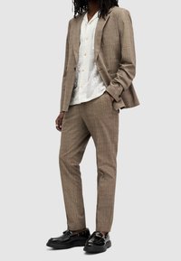 Hnědý kostkovaný oblek s přiléhavým sakem a ušitými kalhotami. Doplněné bílou košilí s krátkým rukávem a černými robustními botami.