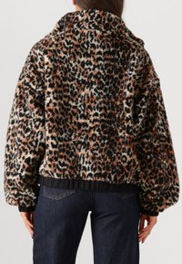 Vrouw in een nepbontjack met luipaardprint in zwart, bruin en wit, gecombineerd met donkerblauwe jeans, gezien van de achterkant.