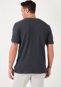 Tricou ribbed gri închis, cu mâneci scurte, guler rotund și o croială lejeră. Prezintă cusături vizibile și un material texturat.