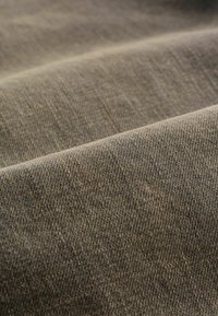 Gros plan sur un tissu doux, texturé, brun-gris avec un motif de tissage subtil et des plis délicats.