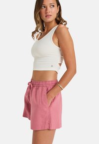 Biely rebrovaný crop tank top v kombinácii s ružovými ľanovými šortkami s elastickým pásom a bočnými vreckami. Jednoduchá, ležérna estetika.