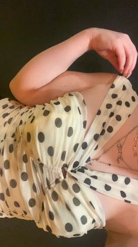 Hvid kjole med fremtrædende sorte prikker, der har en rynket bodice, off-shoulder design og en flydende, blød tekstur.